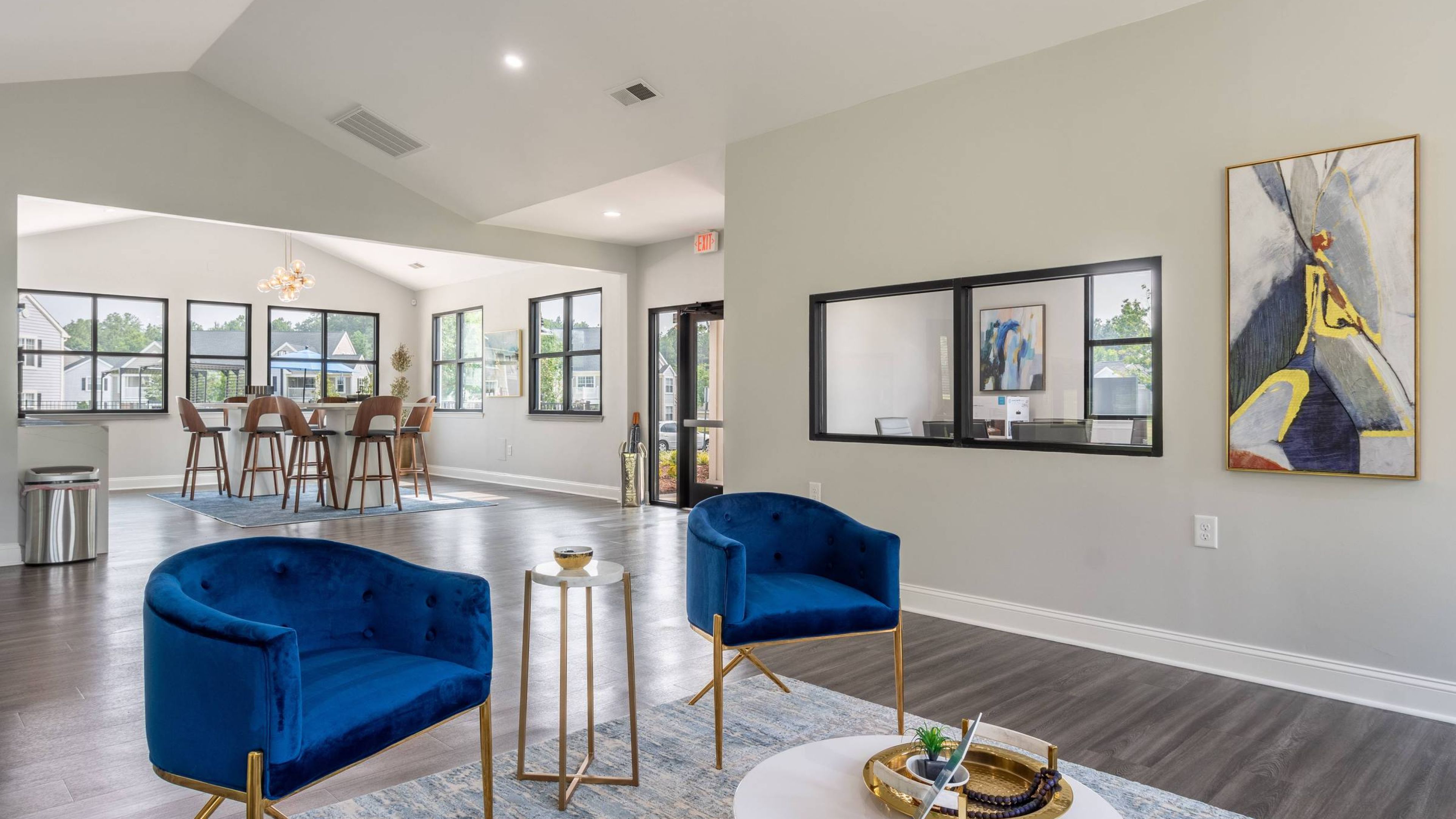 Hawthorne at the Pines modern clubhouse interior with high ceilings, plush blue velvet chairs, and abstract art, overlooking a bright bar area with stools