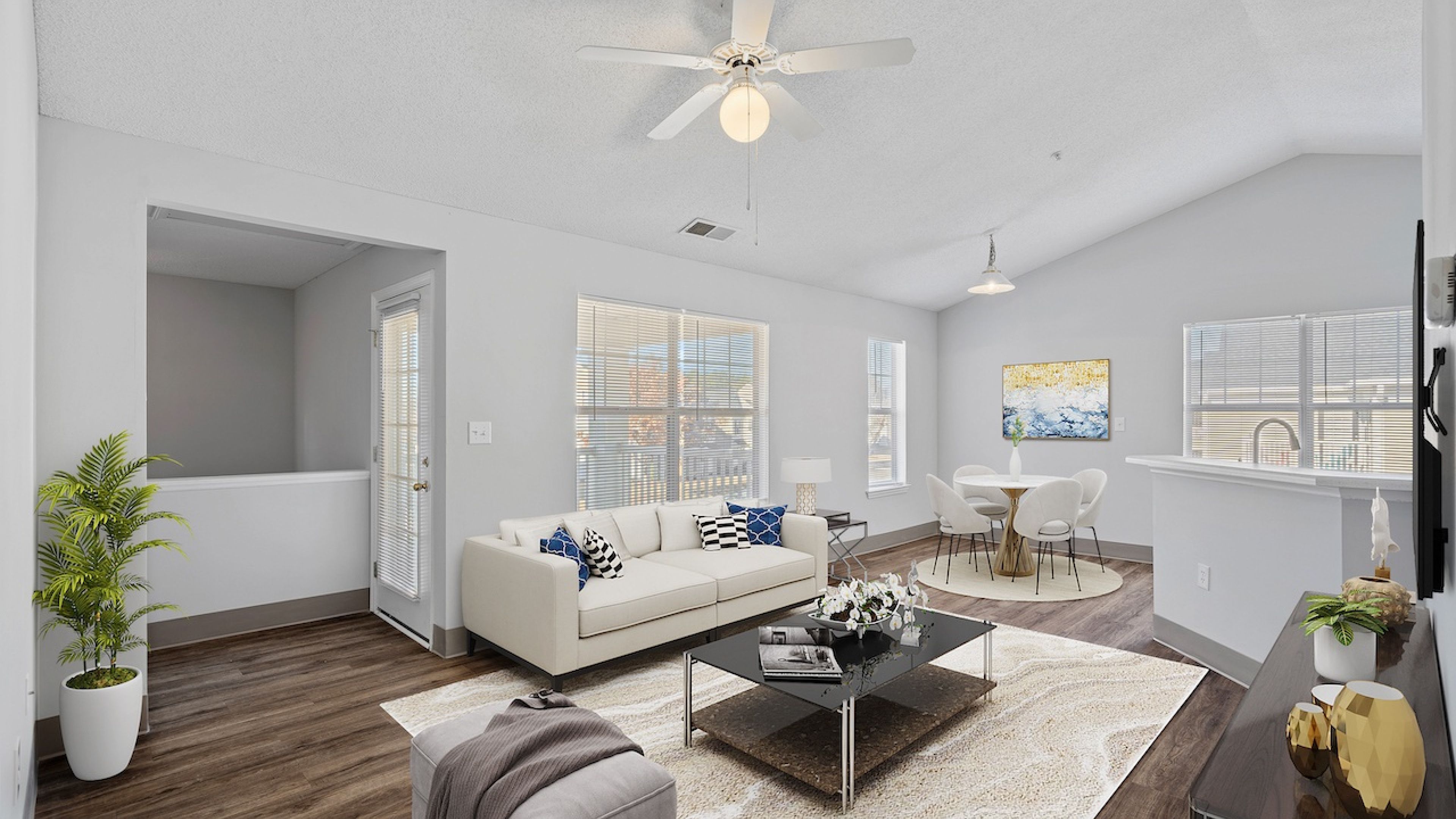 Hawthorne at the Pines spacious living room with high ceiling and ceiling fan, a beige sofa, glass coffee table, and an open dining area in the background