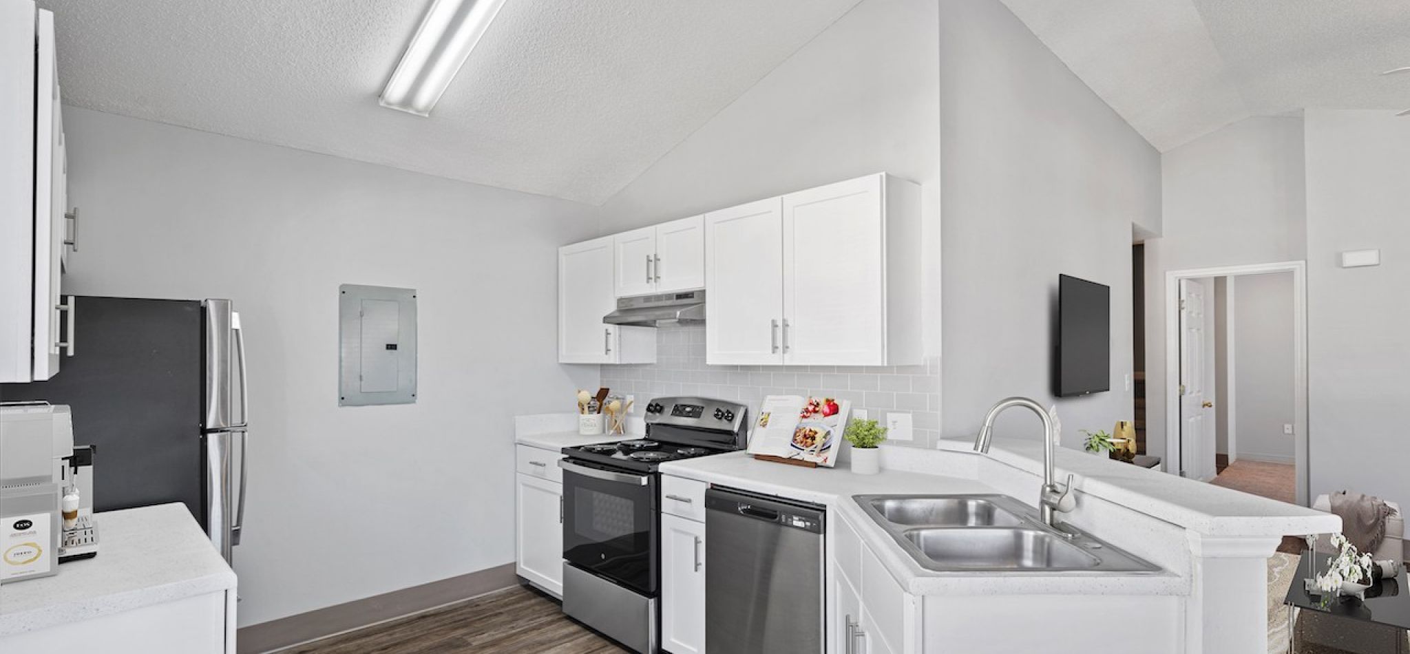 Hawthorne at the Pines bright kitchen space with white cabinets, stainless steel appliances, and a subway tile backsplash, with a flat-screen TV on the wall